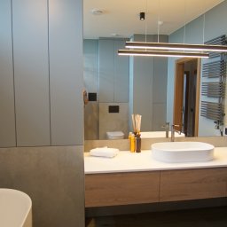 DesignLAB Manufaktura Mebli - Nowoczesna łazienka z umywalką nablatową, drewnianą szafką pod umywalką i grzejnikiem drabinkowym. Duże lustro odbija dalszą część łazienki.