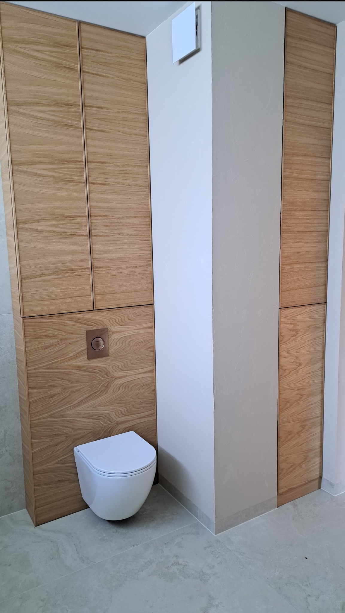 Nowoczesna łazienka z drewnianymi szafkami na wymiar w zabudowie, wisząca toaleta i minimalistyczny design. Widoczne detale wykończenia i armatura.