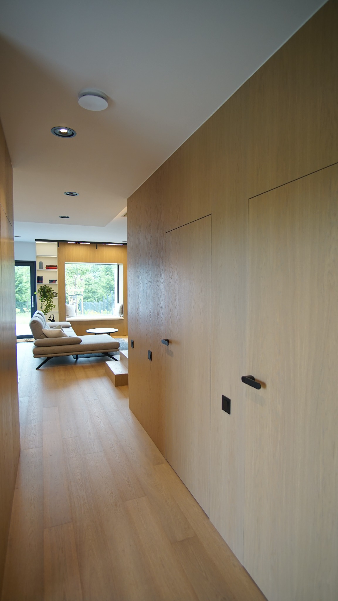 Nowoczesne wnętrze z zabudową drewnianą i ukrytymi drzwiami w Marcinkowicach. Minimalistyczny design, jasne drewno i subtelne oświetlenie.