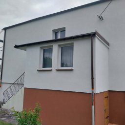 Pro-System Łukasz Kloskowski - Odnowiona elewacja budynku z brązowym akcentem w dolnej części, widoczne rusztowania. Usługi remontowe w Człuchowie.