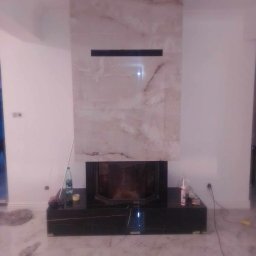 Pro-System Łukasz Kloskowski - Wykończony kominek z marmurową obudową i czarną podstawą, widoczne akcesoria montażowe. Nowoczesny design, jasne wnętrze.