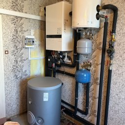 OSAINSTAL Bartosz Osowicki - Zestaw urządzeń grzewczych: piec, zasobnik ciepłej wody, zbiorniki wyrównawcze, rury w izolacji. Montaż w pomieszczeniu z tapetą w kwiaty.