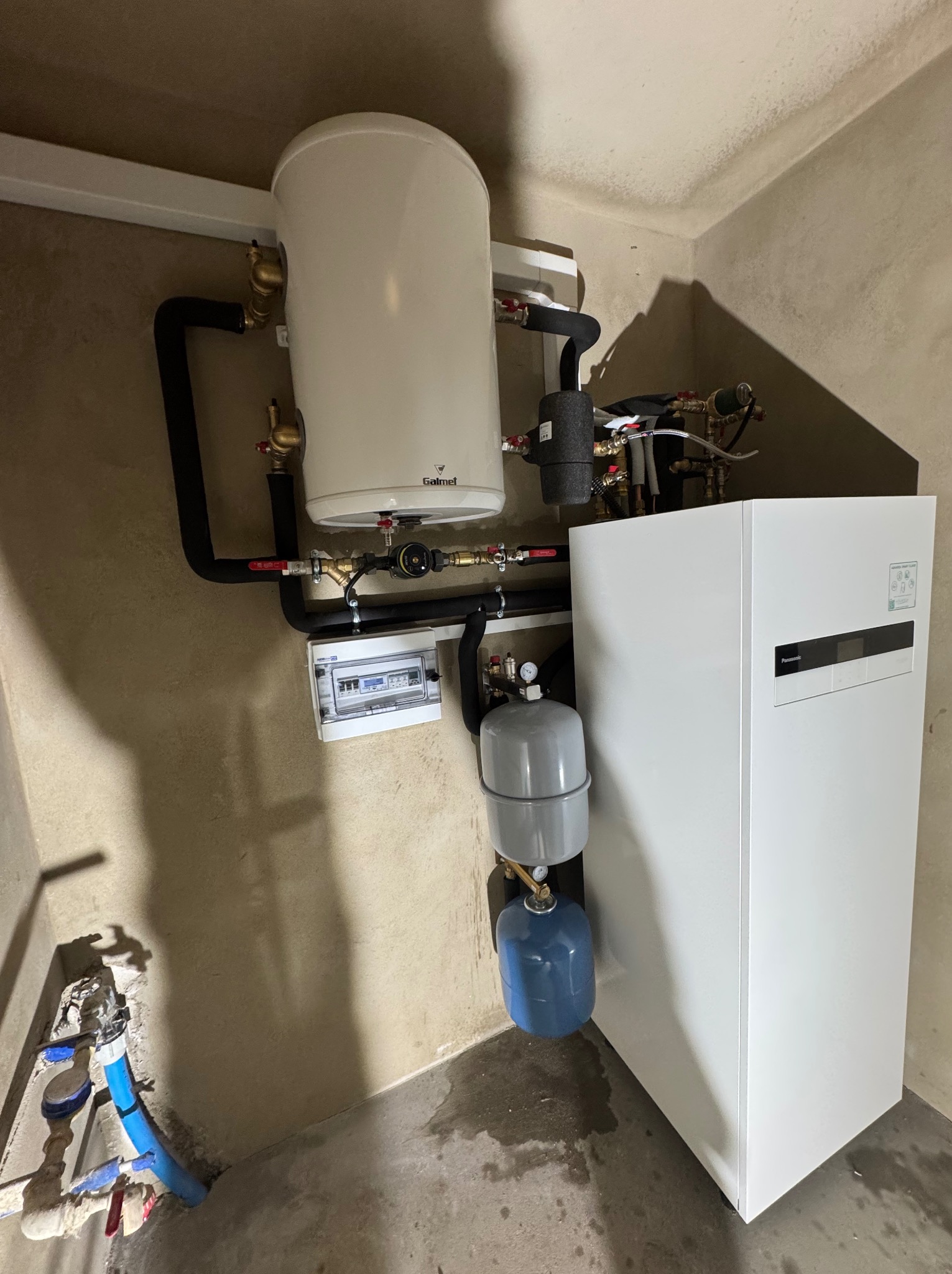 Zmontowana instalacja CO z piecem gazowym, zbiornikiem i osprzętem. Widoczne rury, zawory, manometry i skrzynka elektryczna. Ściany w surowym stanie.