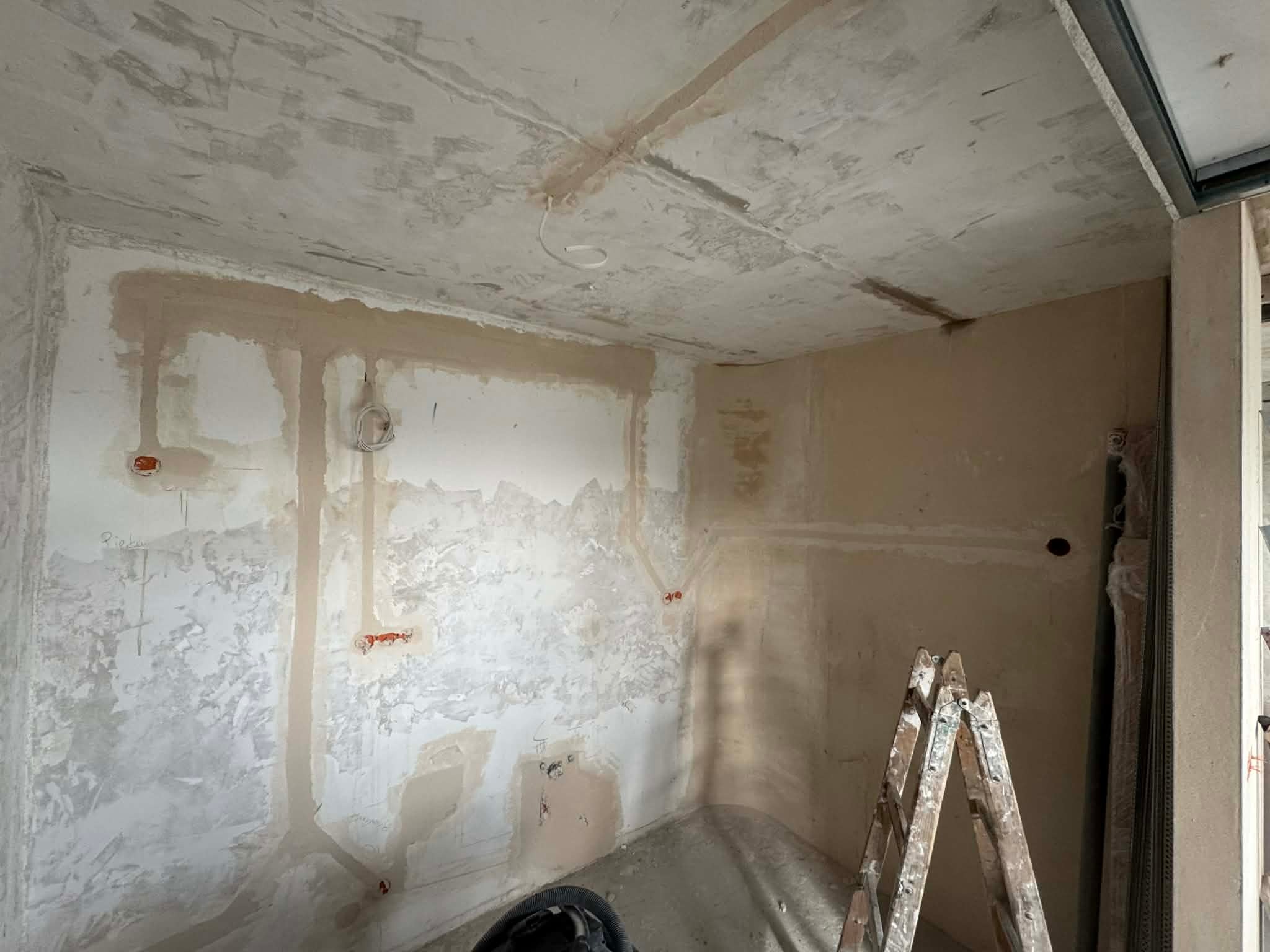 Prace przygotowawcze do instalacji elektrycznej w Krakowie. Widoczne kable w ścianach, surowy tynk i drabina malarska. Etap przed wykończeniem.