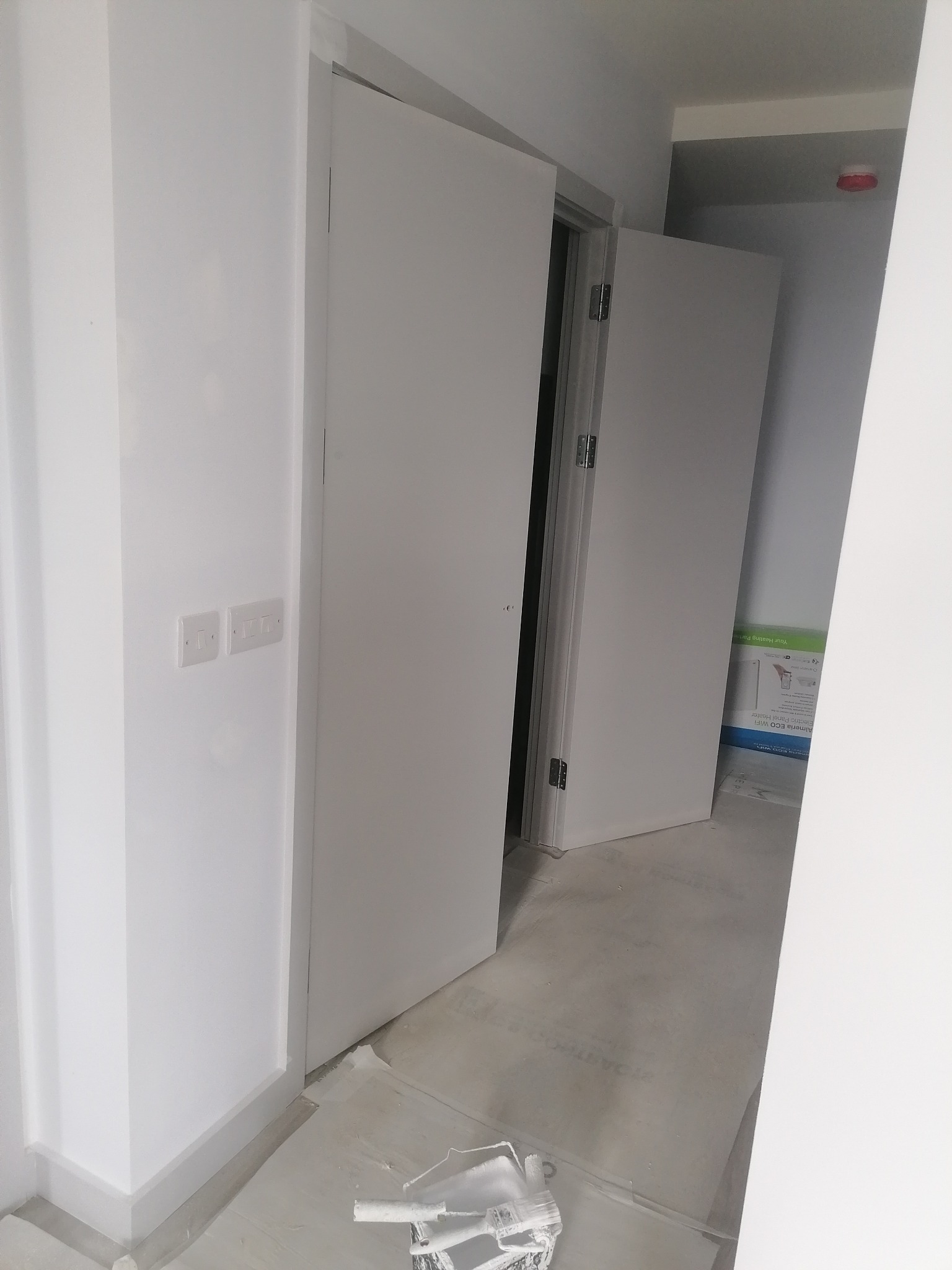 Wnętrze po odświeżeniu: białe ściany, drzwi i listwy przypodłogowe. Na podłodze widoczne narzędzia malarskie, sugerujące niedawno zakończone prace wykończeniowe.