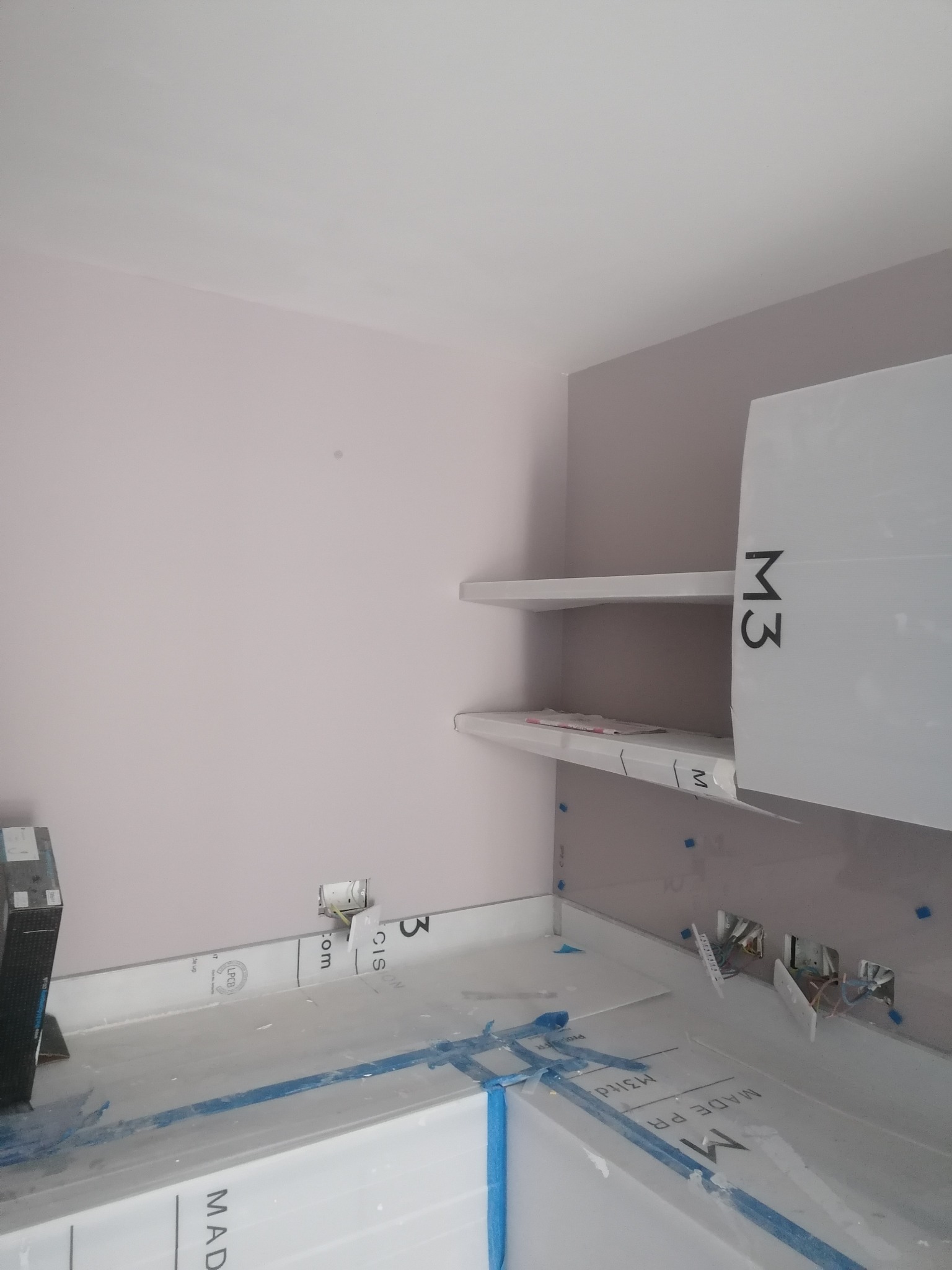 Świeżo pomalowane ściany w odcieniach szarości i fioletu w pomieszczeniu z półkami i instalacją elektryczną, zabezpieczone folią meble.