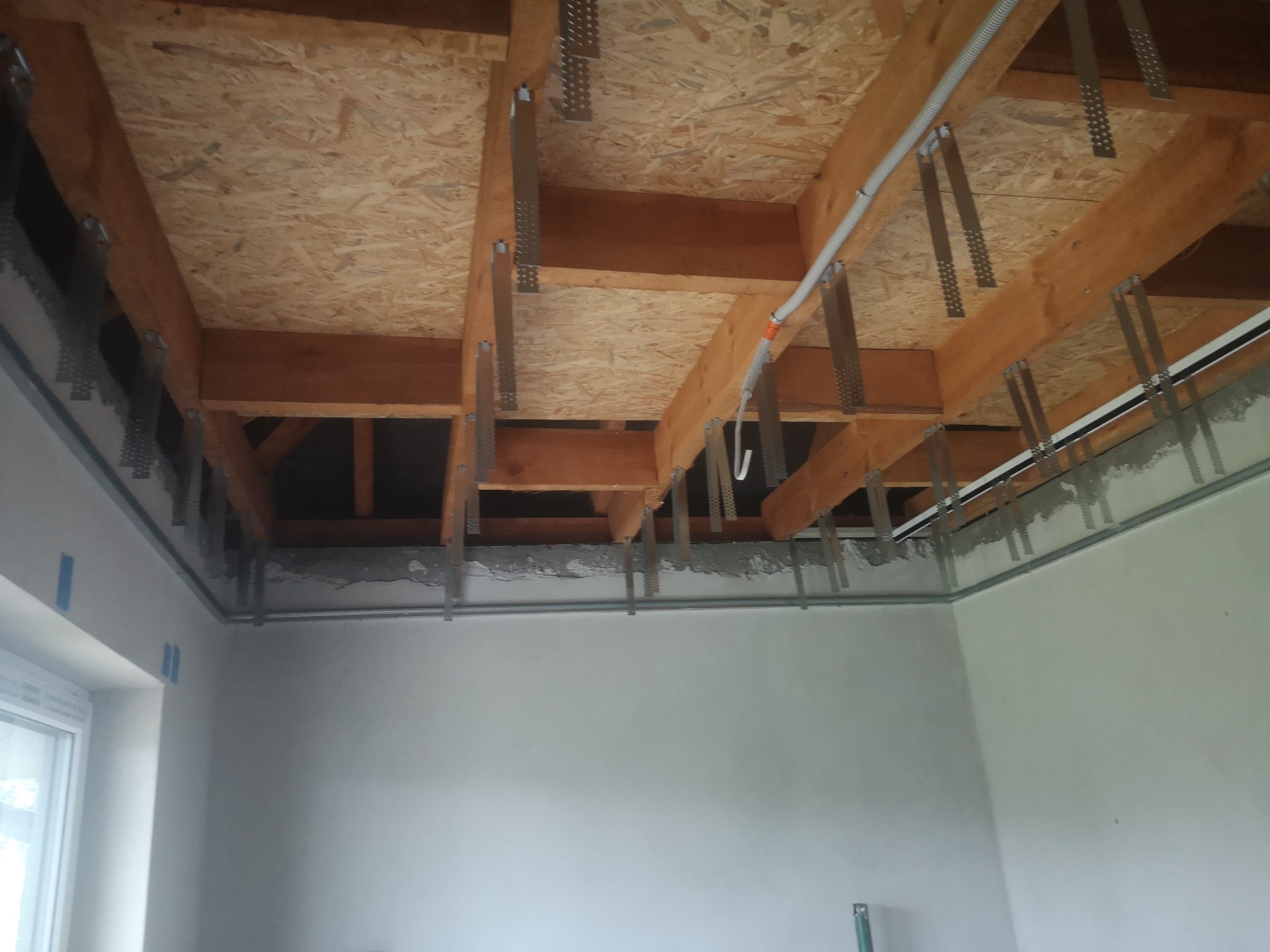 Sufit podwieszany w trakcie montażu: drewniana konstrukcja z płyt OSB, metalowe profile i instalacja elektryczna. Widok z dołu na surowy stan wykończenia.