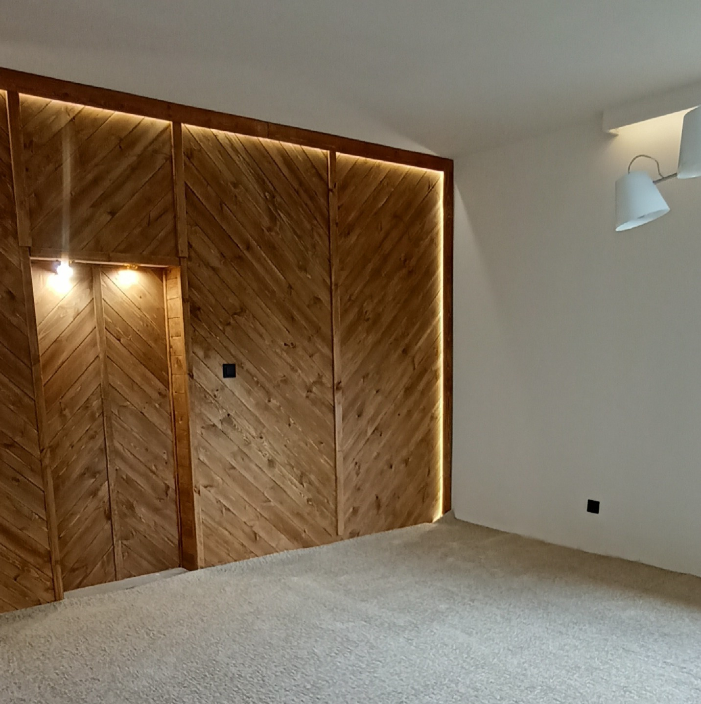 Drewniana ściana z oświetleniem LED w jodełkę, czarny włącznik, biała ściana z lampą, jasna podłoga, nowoczesny design, ciepłe światło.