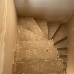 Slawbud - Wnętrze w trakcie prac wykończeniowych: schody i ściany pokryte świeżym tynkiem. Widoczne buty pracownika, co sugeruje trwający remont.