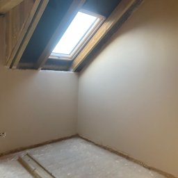Slawbud - Pokój na poddaszu po nałożeniu gładzi, widoczne drewniane elementy konstrukcji dachu i okno dachowe. Ściany gładkie, przygotowane do malowania.