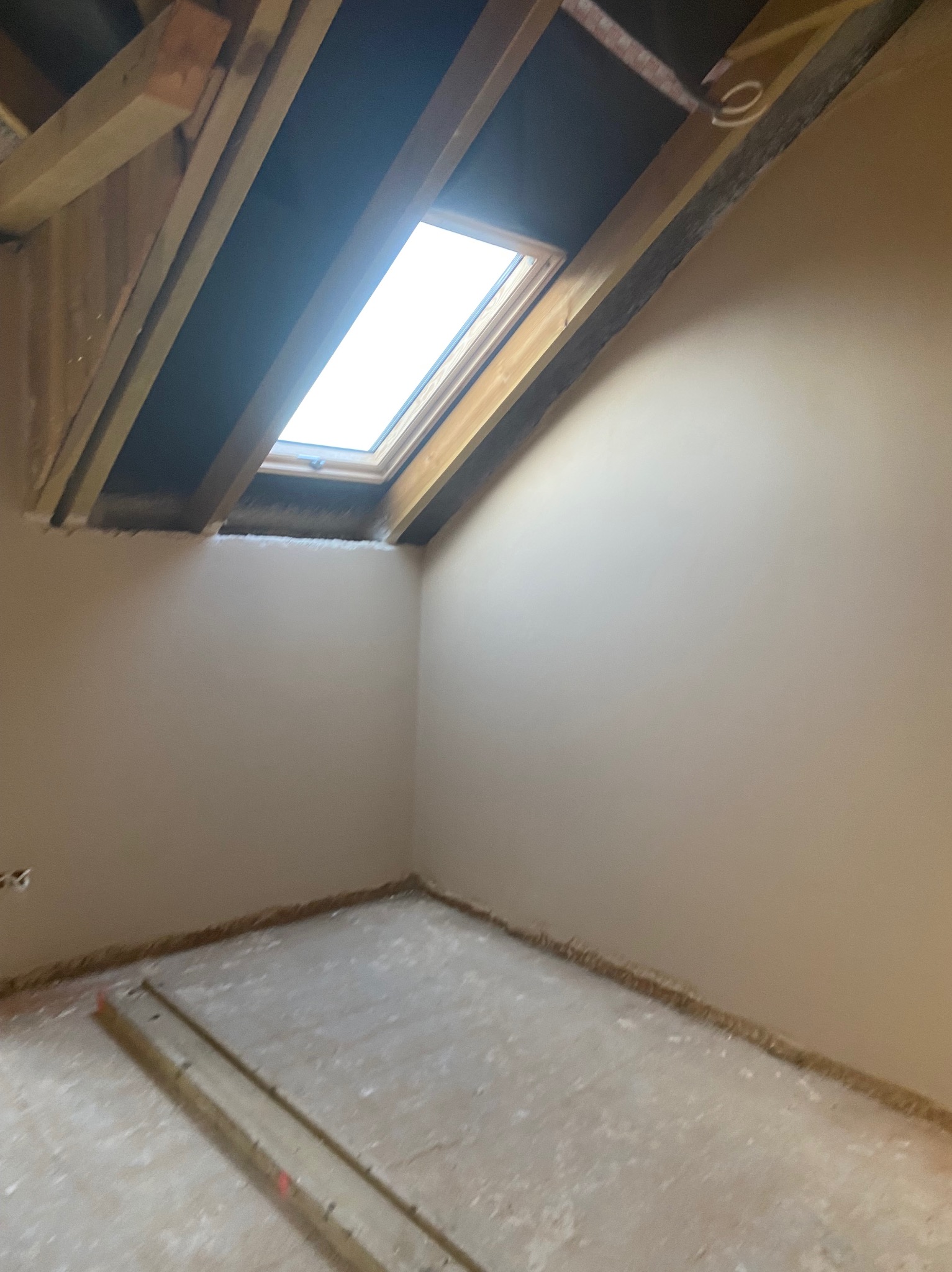 Pokój na poddaszu po nałożeniu gładzi, widoczne drewniane elementy konstrukcji dachu i okno dachowe. Ściany gładkie, przygotowane do malowania.