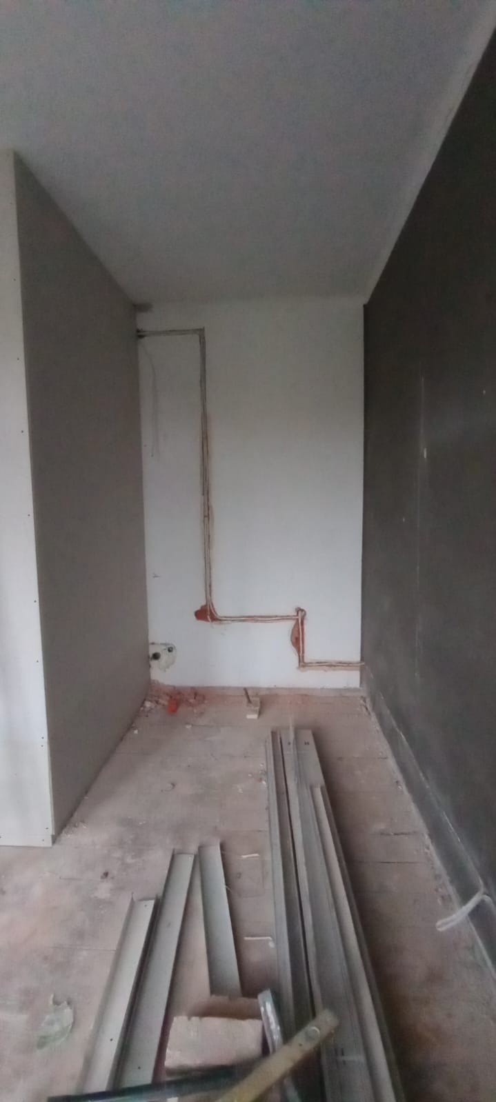 Wykute bruzdy w ścianie pod instalację elektryczną podtynkową. Widoczne kable w peszlach, fragmenty listew przypodłogowych na podłodze. Surowy stan wykończenia.