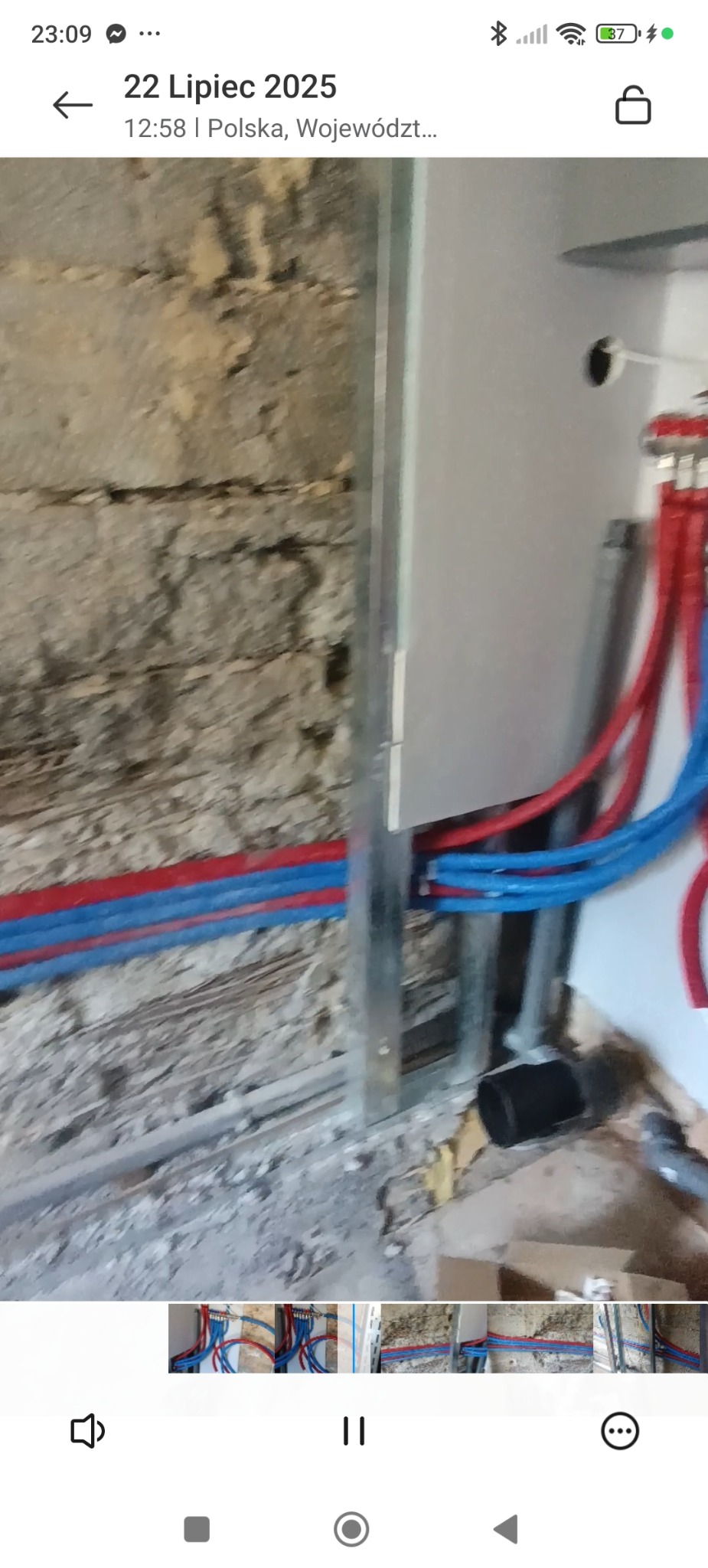 Instalacja wodna z rurami PEX w kolorach czerwonym i niebieskim, zamontowana na ścianie z surowej cegły, obok metalowej konstrukcji. Widoczny etap prac wykończeniowych.