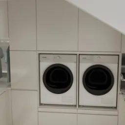 Funkcjonalna pralnia w zabudowie: pralka, suszarka, deska do prasowania i wieszak na ubrania. Minimalistyczny design w jasnych, stonowanych barwach.