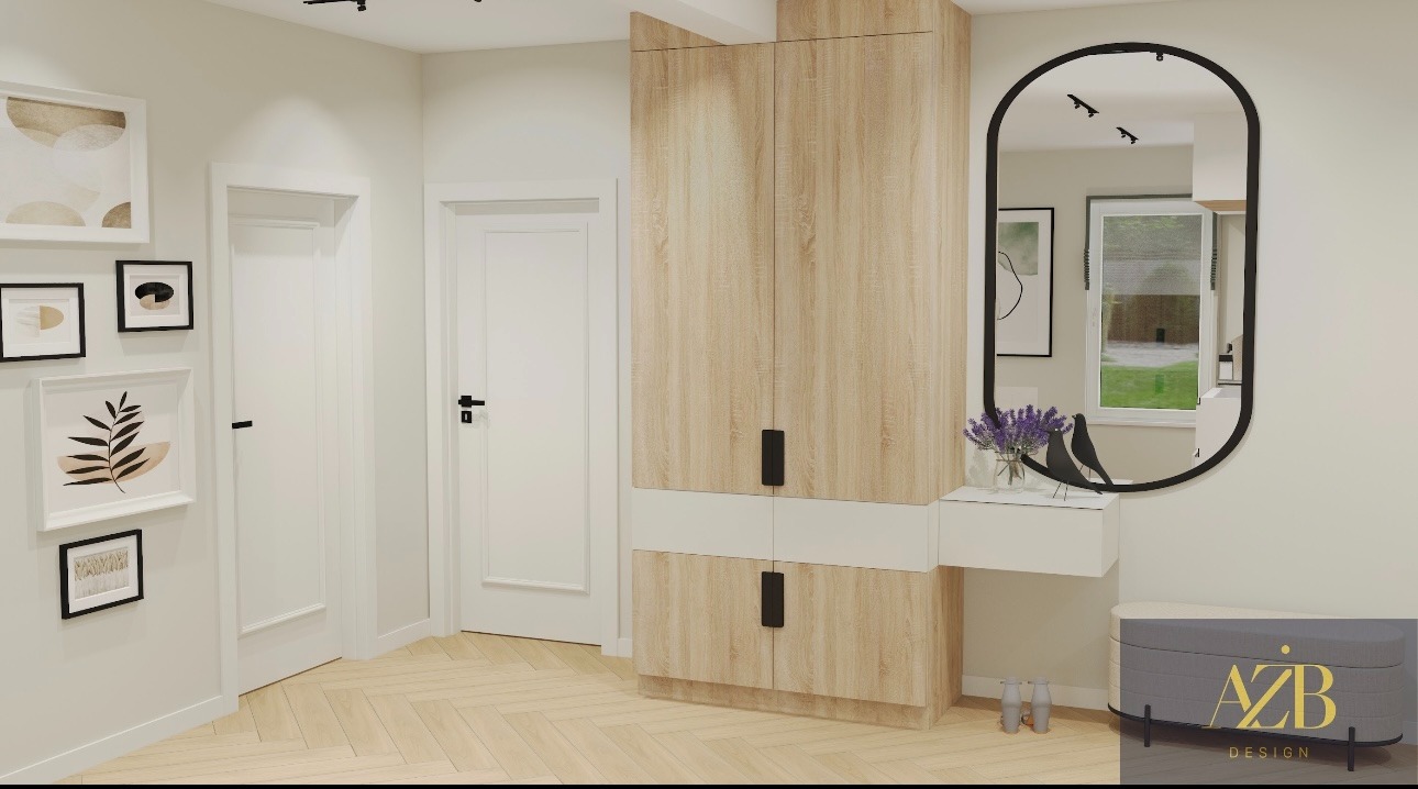 Wnętrze przedpokoju z drewnianą szafą, lustrem w czarnej ramie i galerią obrazów na ścianie. Podłoga z jasnej klepki ułożonej w jodełkę. Minimalistyczny design.