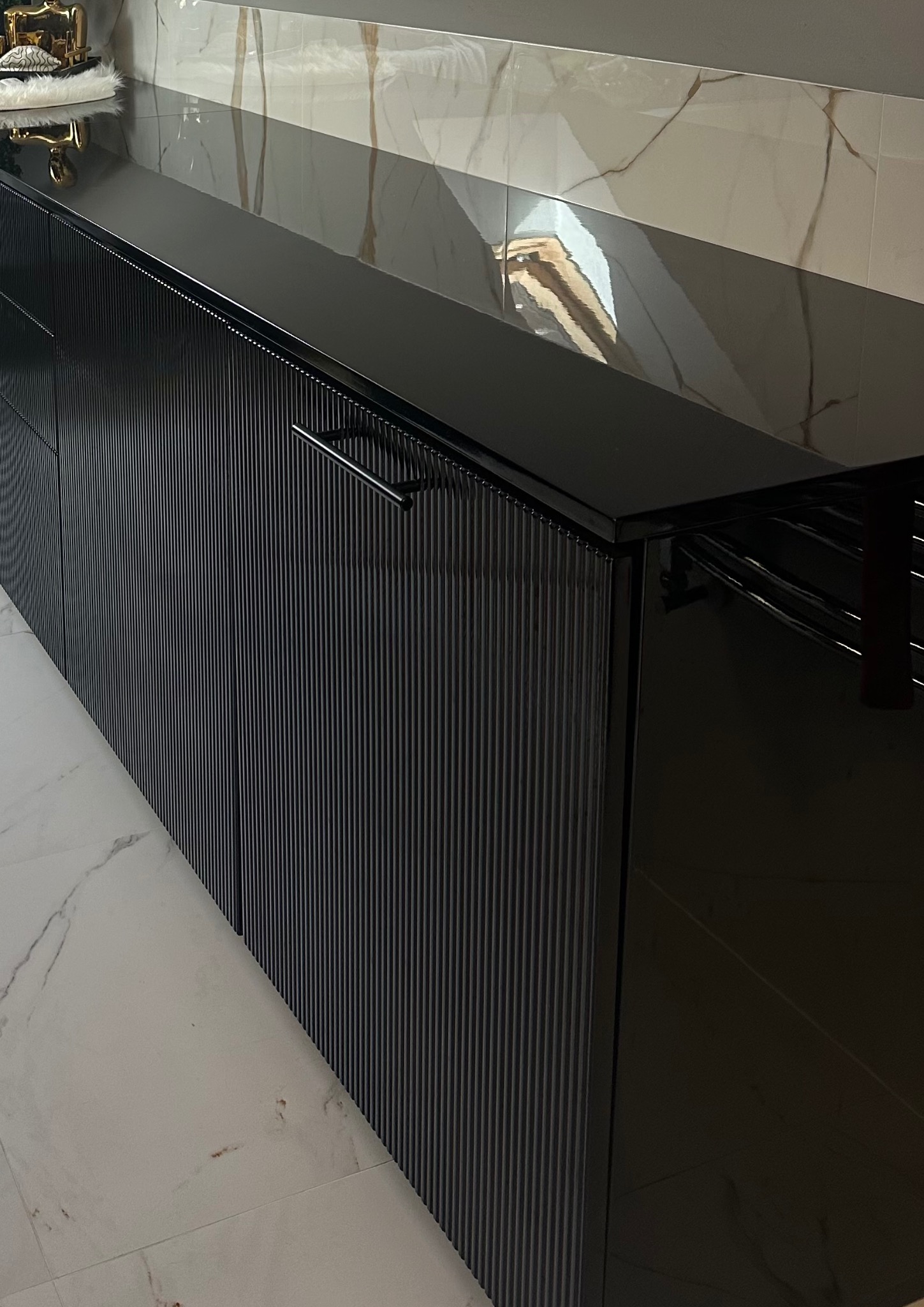 Czarne, ryflowane fronty szafek kuchennych z połyskiem, marmurowy blat i płytki. Minimalistyczny design z metalowymi uchwytami. Nowoczesna kuchnia na wymiar.