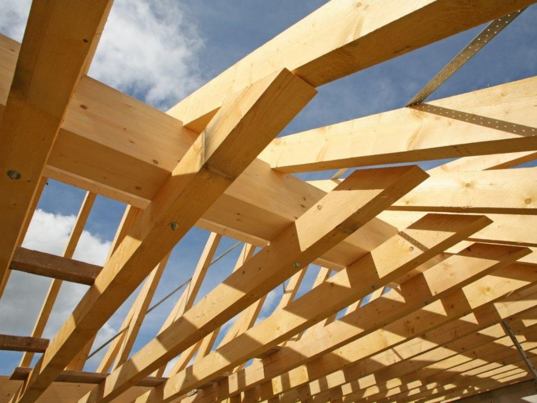 Konstrukcja drewniana dachu w trakcie budowy, widok z dołu na jasne belki i niebo. Elementy złączone metalowymi płytkami.