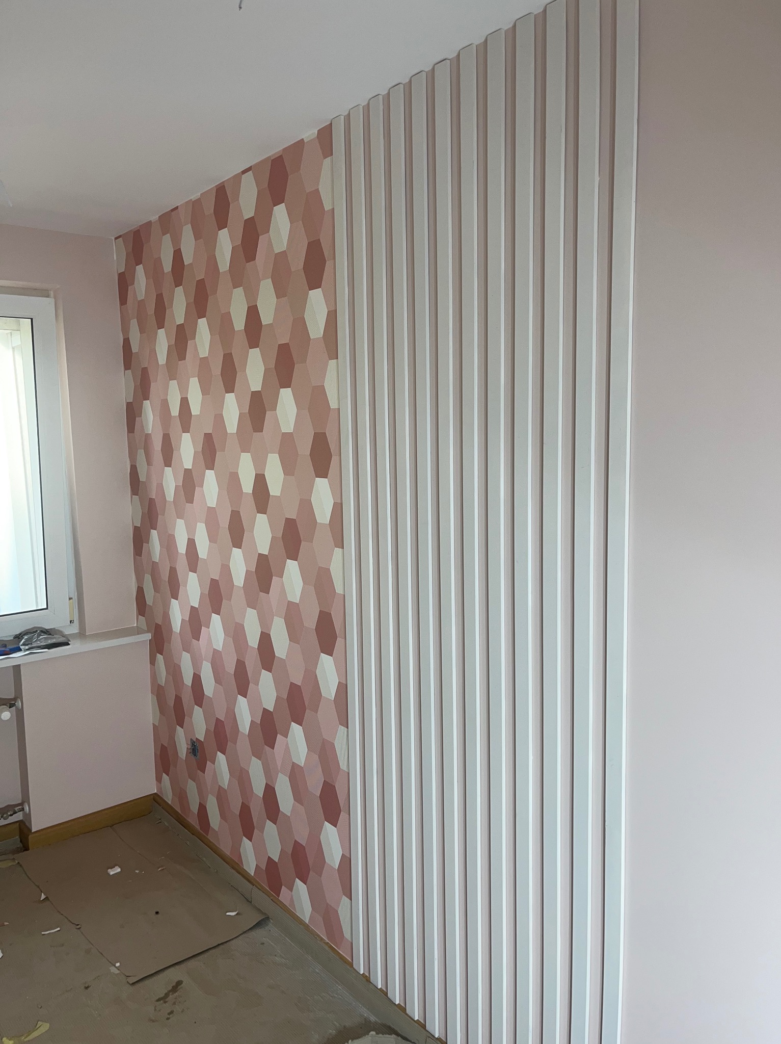Ściana w pokoju po remoncie: dekoracyjna tapeta w geometryczne wzory i pionowe, białe lamele. Podłoga zabezpieczona kartonem.