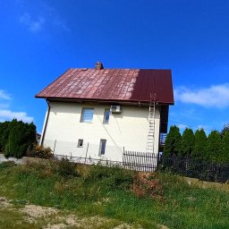 ATADOM SPÓŁKA Z OGRANICZONĄ ODPOWIEDZIALNOŚCIĄ - Dom z częściowo pomalowanym na ciemny brąz dachem, drabina oparta o ścianę. Widoczny kontrast między starą a nową powłoką. Błękitne niebo w tle.