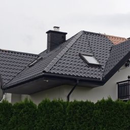 ATADOM SPÓŁKA Z OGRANICZONĄ ODPOWIEDZIALNOŚCIĄ - Ciemny dach z dachówką falistą i oknami połaciowymi, widoczny fragment elewacji i rynna. Na pierwszym planie żywopłot z tui.