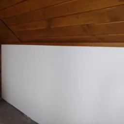 Biała ściana w pomieszczeniu z drewnianym sufitem i fragmentem ceglanej ściany. Widoczne łączenie sufitu ze ścianą. Kąt ujęcia z dołu.