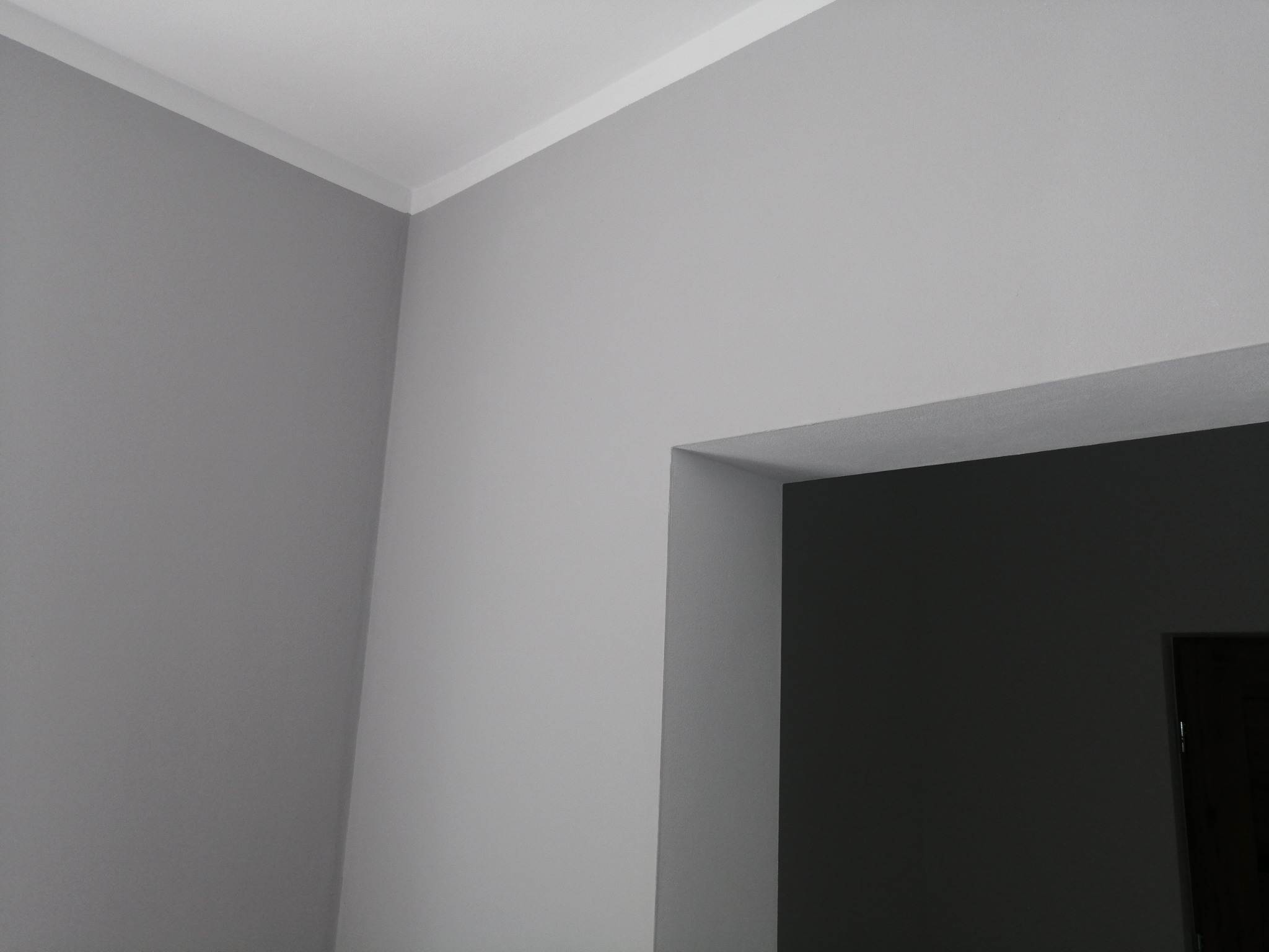 Pomieszczenie po malowaniu na szaro, widoczna listwa przysufitowa i fragment ściany przy wejściu do innego pokoju pomalowanego na ciemniejszy kolor.