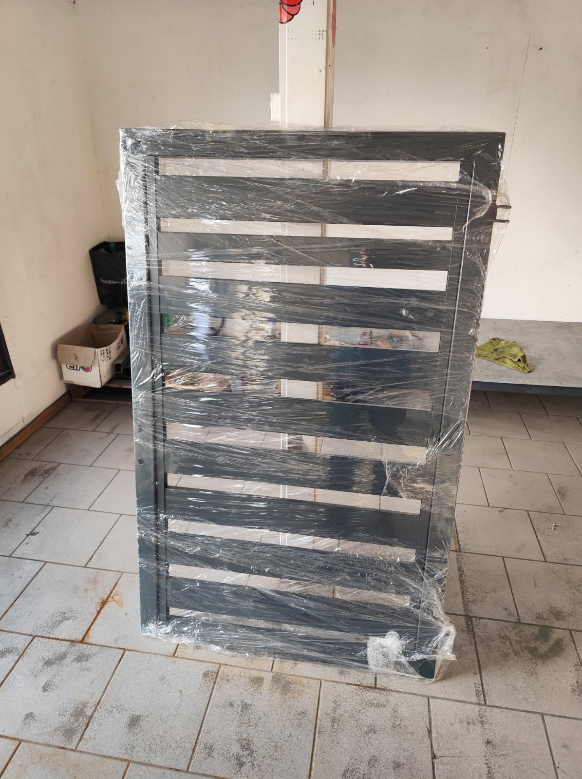 Nowa, metalowa brama panelowa w folii ochronnej, gotowa do montażu. Widok z bliska na poziomym kafelkowanym podłożu. Minimalistyczny design z poziomymi szczeblami.