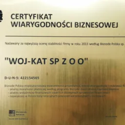 Certyfikat Wiarygodności Biznesowej dla 'WOJ-KAT SP Z O O' od Bisnode Polska, przyznany za stabilność firmy w 2013 roku. Złota tablica z logo i danymi firmy.