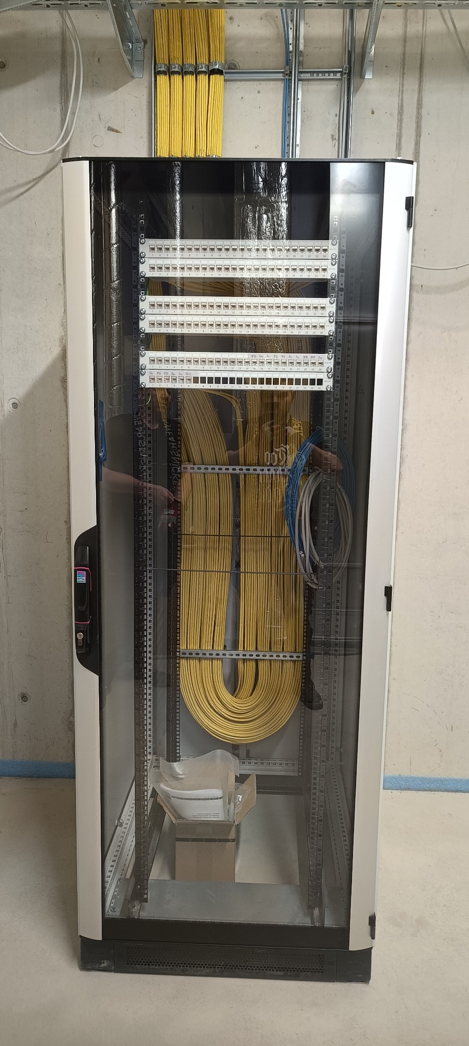 Szafa rack z uporządkowanymi kablami ethernetowymi w kolorze żółtym i niebieskim, widoczne panele krosownicze i okablowanie strukturalne wewnątrz szafy.