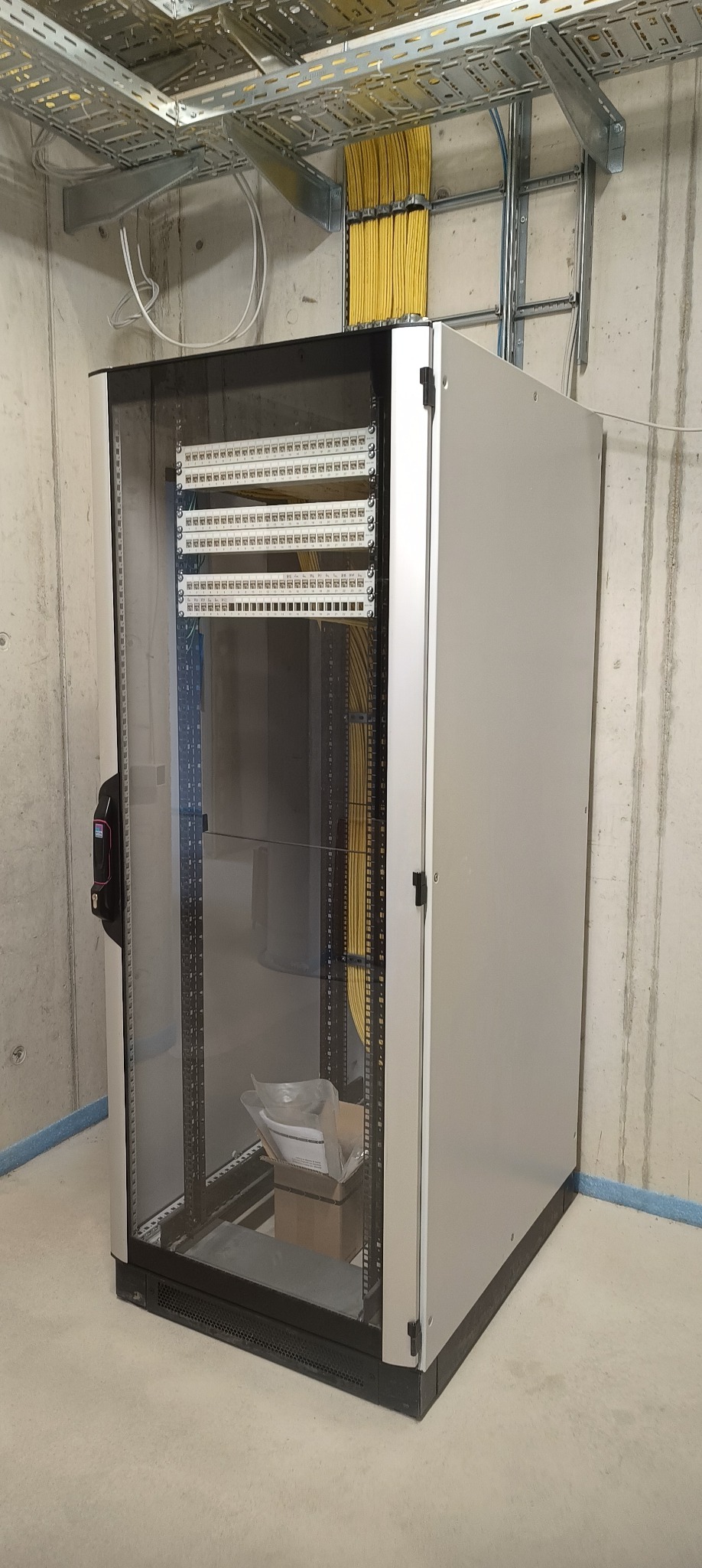 Szafa serwerowa z okablowaniem w Dąbrówce Łubniańskiej. Żółte kable ułożone w korytkach pod sufitem. Widoczne panele krosownicze. Nowa instalacja.