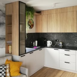 Gawra Studio Projektowe Justyna Miś-Nalepka - Nowoczesna kuchnia z drewnianymi szafkami górnymi i białymi dolnymi. Na blacie czajnik, akcesoria kuchenne, kwiaty doniczkowe. Parkiet na podłodze.