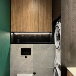 Gawra Studio Projektowe Justyna Miś-Nalepka - Nowoczesna łazienka z zabudową meblową z drewna, szarą płytką imitującą marmur i zieloną ścianą. Widoczna toaleta podwieszana i pralka z suszarką w zabudowie.