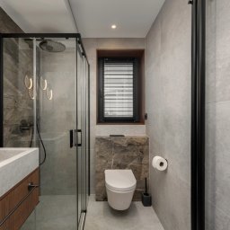 Gawra Studio Projektowe Justyna Miś-Nalepka - Nowoczesna łazienka z kabiną prysznicową typu walk-in, wiszącą toaletą i grzejnikiem drabinkowym w czarnym kolorze. Ściany wyłożone szarą płytką, akcenty z kamienia.