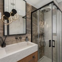 Gawra Studio Projektowe Justyna Miś-Nalepka - Nowoczesna łazienka z kabiną prysznicową typu walk-in, umywalką z kamienia na drewnianej szafce i lustrem z designerskim oświetleniem. Płytki imitujące marmur.