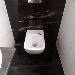 Mykola Kreshchyk - Nowoczesna toaleta podwieszana z czarną, marmurkową okładziną ścian i podłogi, uzupełniona o białe panele boczne. Minimalistyczny design z chromowanym przyciskiem spłukiwania.