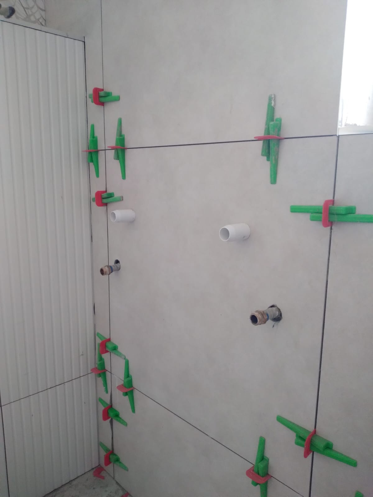 Ściana w trakcie układania płytek z użyciem klipsów poziomujących w Poznaniu. Widoczne otwory na instalacje i białe płytki.