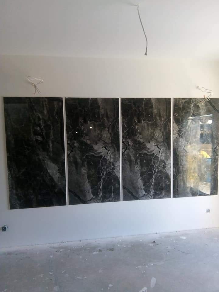 Cztery czarne, marmurowe płyty ścienne z białymi fugami, tworzące panel dekoracyjny w surowym wnętrzu z widocznymi przewodami elektrycznymi.