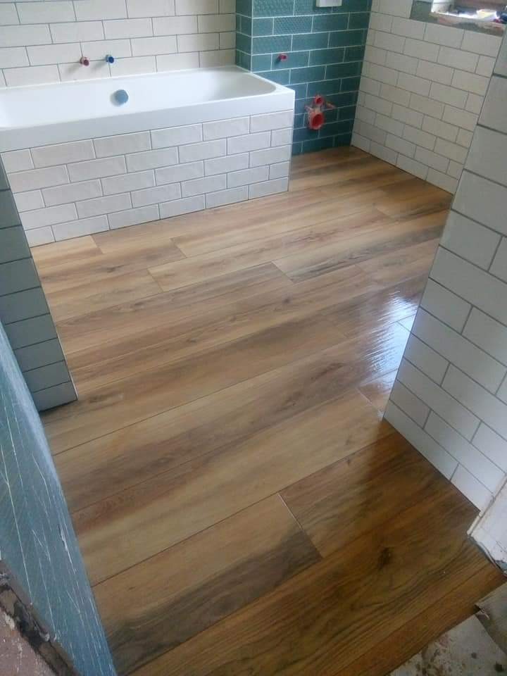 Wykończona łazienka z drewnopodobną podłogą, białą wanną obłożoną kafelkami i częściowo zieloną ścianą z płytek. Widok z poziomu podłogi, ukośne ujęcie.