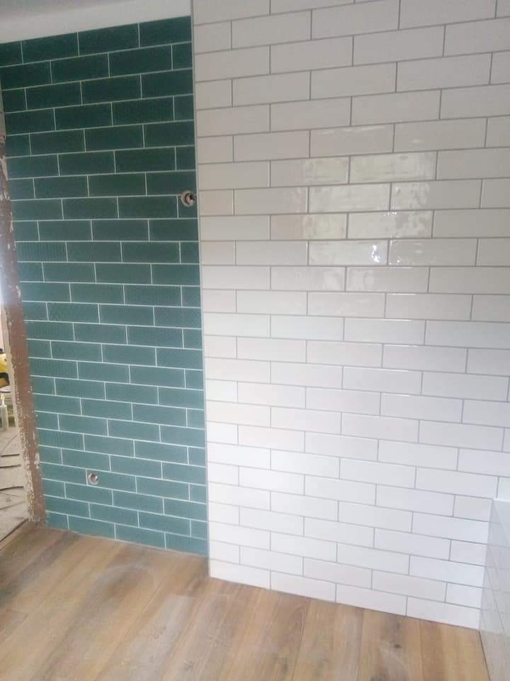 Ściana wyłożona dwukolorowymi, prostokątnymi płytkami (zieleń i biel) w stylu cegiełki. Widoczne gniazdka elektryczne. Podłoga drewniana.