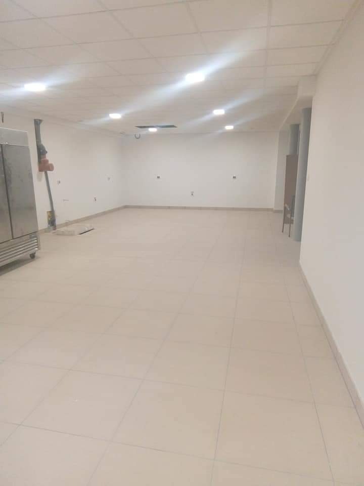 Wnętrze komercyjne z wyłożoną podłogą z płytek, przygotowane do dalszych prac wykończeniowych. Widoczna instalacja na ścianie i fragment wyposażenia.