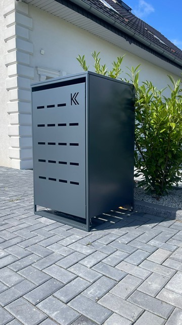 Nowoczesna, antracytowa pergola metalowa z perforowanym panelem bocznym, umieszczona na brukowanym podjeździe przed domem. Minimalistyczny design.