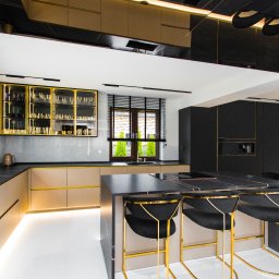 Luxwood Atelier - Nowoczesna kuchnia: beżowe szafki z złotymi akcentami, czarny blat i wyspa z hokerami. Marmurowa ściana i oświetlenie LED. Minimalistyczny design z luksusowymi detalami.