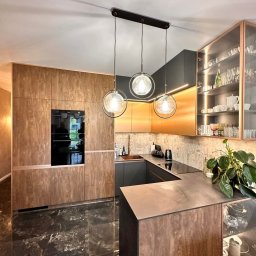 Luxwood Atelier - Nowoczesna kuchnia z marmurową podłogą, drewnianymi frontami, szarymi elementami i trzema okrągłymi lampami wiszącymi. Szkło i oświetlenie w szafkach.