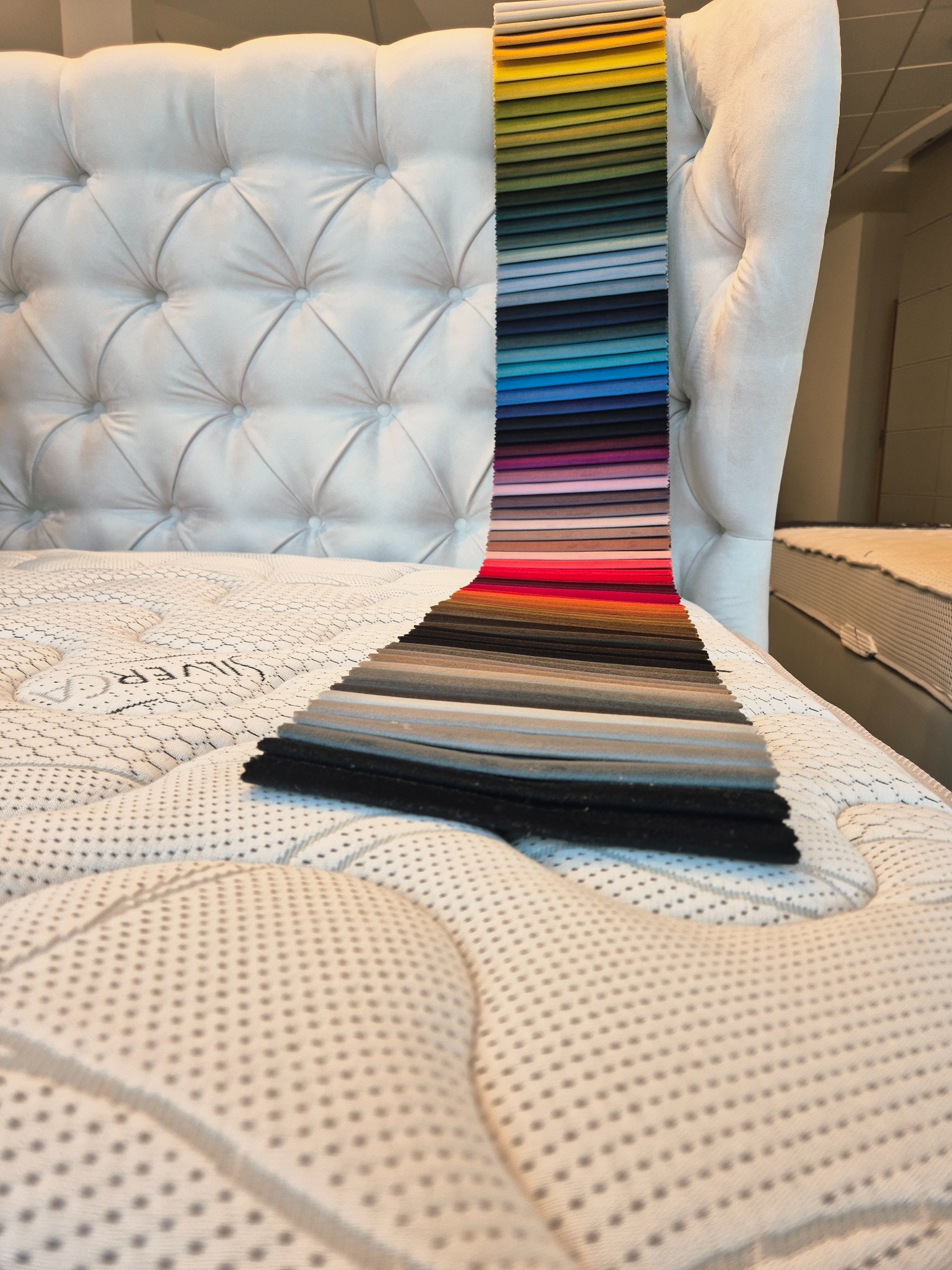 Tapicerowany zagłówek łóżka z próbkami tkanin w różnych kolorach. Detal prezentujący wybór materiałów obiciowych do mebli na wymiar.