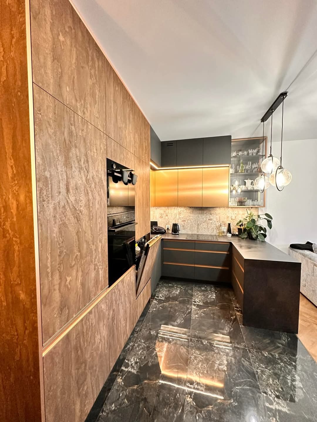 Nowoczesna kuchnia w odcieniach brązu i szarości z marmurową podłogą i oświetleniem LED, widok z perspektywy podłogi. Fronty szafek z efektem kamienia.