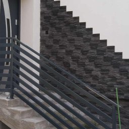 Lidia Tadych - Schody wejściowe z szarą balustradą i dekoracyjną, ciemną okładziną elewacyjną ułożoną schodkowo. Nowoczesne wykończenie zewnętrzne budynku.