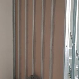 Lidia Tadych - Konstrukcja ścianki działowej z płyt kartonowo-gipsowych na metalowym stelażu. Widoczny fragment drabiny i torba robocza. Etap prac wykończeniowych.