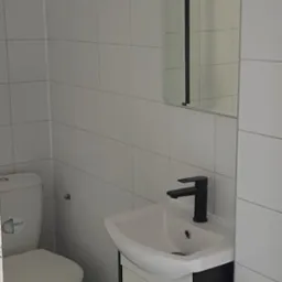 Biała łazienka w Kleszczynie z toaletą, umywalką z szafką i lustrem. Minimalistyczny design, czarna bateria umywalkowa, białe płytki na ścianach.