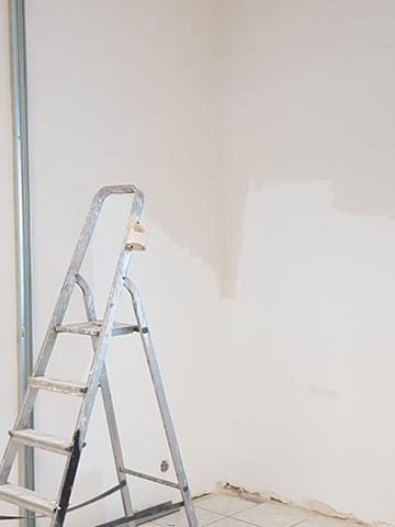 Ściana połatana gładzią, z metalowym profilem i drabiną. Przygotowanie do malowania. Fragment podłogi z resztkami kleju. Ujęcie z dołu, blisko ściany.