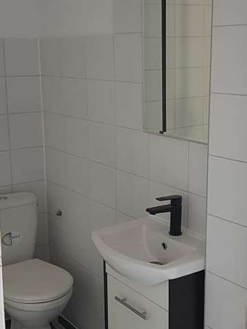 Biała łazienka w Kleszczynie z toaletą, umywalką z szafką i lustrem. Minimalistyczny design, czarna bateria umywalkowa, białe płytki na ścianach.